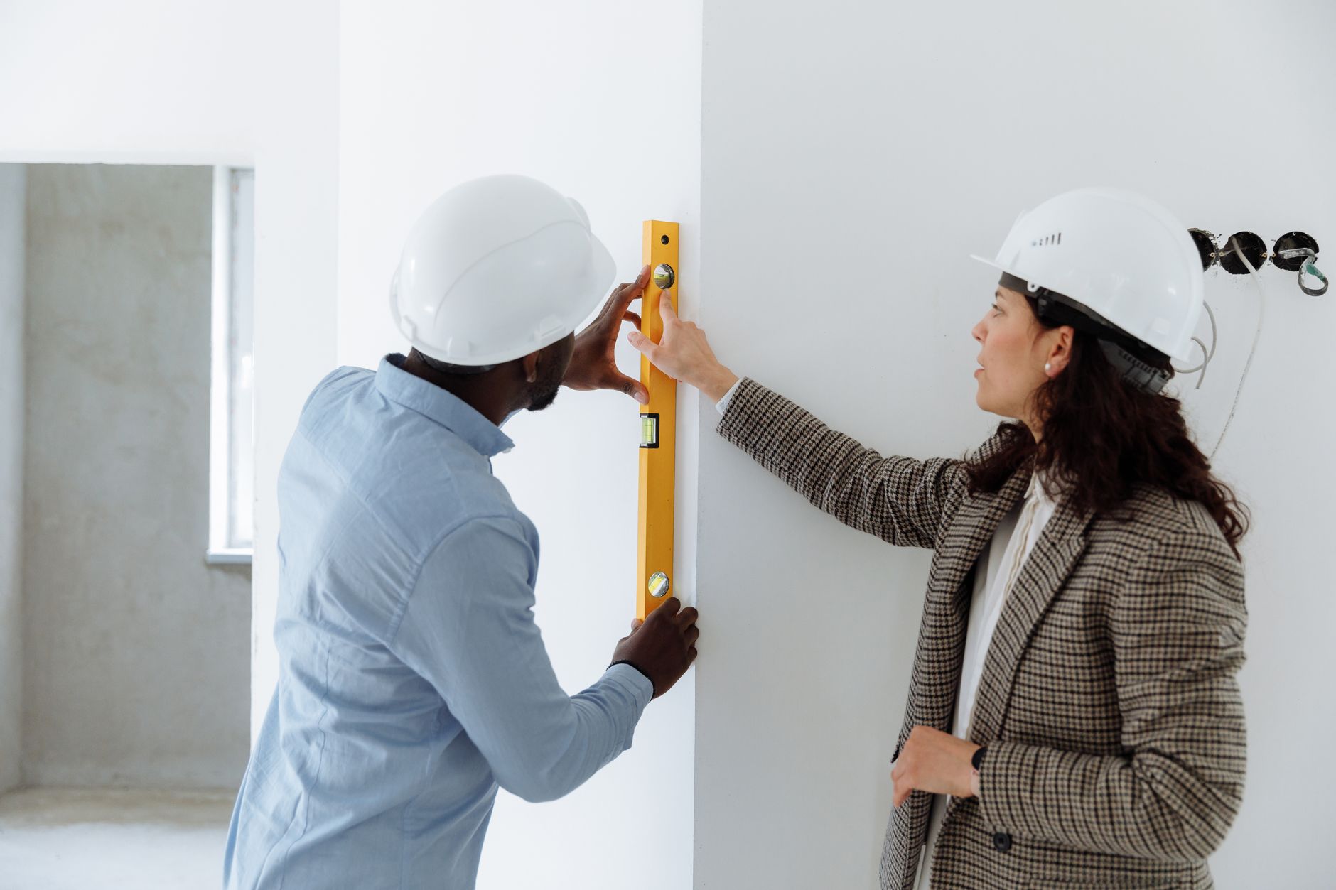 Two people in hard hats checking a wall corner with a yellow level