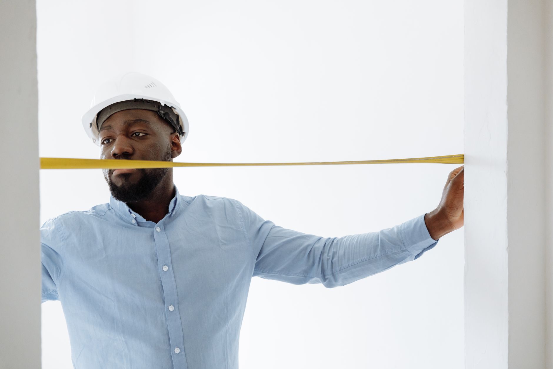 Worker in a hard hat measuring a doorway opening with a yellow tape measure