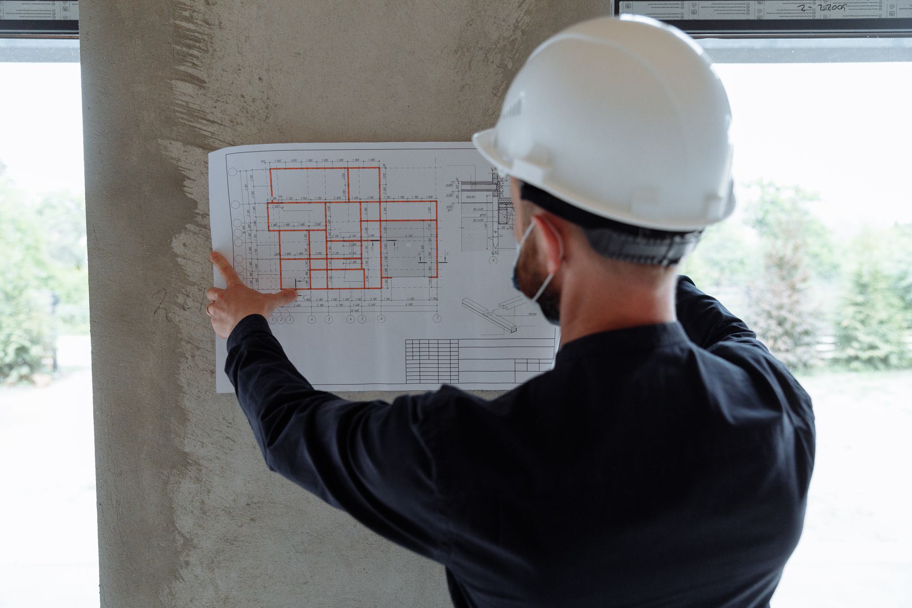 Person in a hard hat reviewing architectural floor plans pinned to a wall